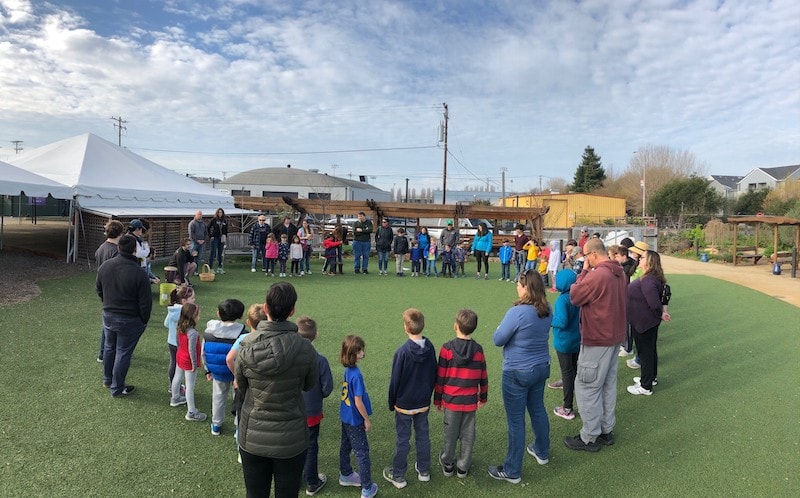Kids and adults standing in a circle on a grassy field